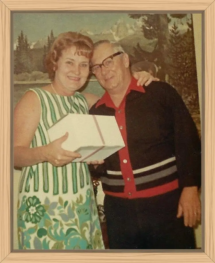 My parents are smiling and my mom has her arm around my dad's shoulder. They are holding a box with a corsage my date gave me that evening for prom. They look happy.