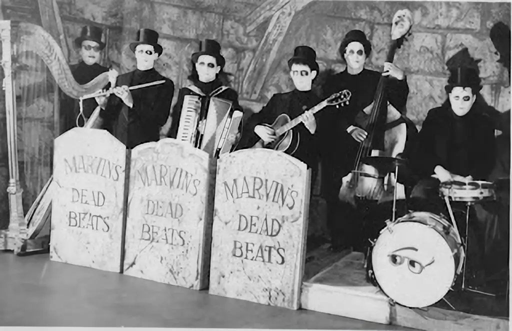 The band of six musicians playing their instruments dressed all in black with top hats and creepy makeup