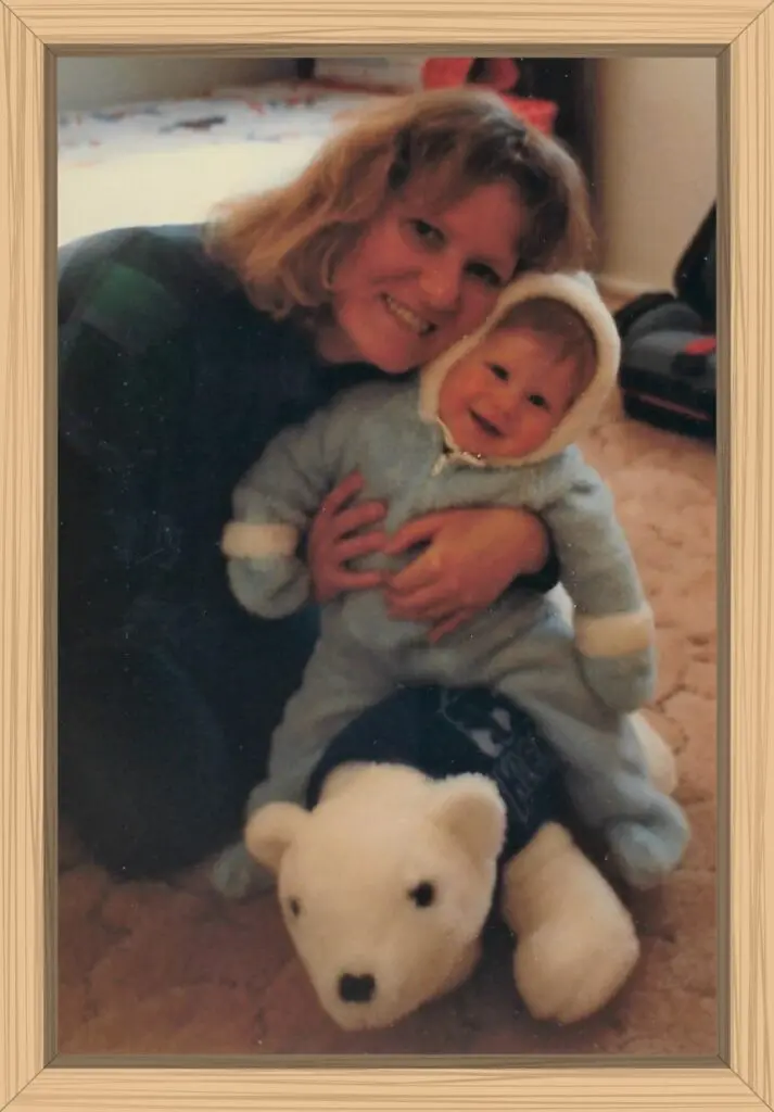 I am hugging Hayes in his snowsuit while he sits on the top of a large white polar bear.