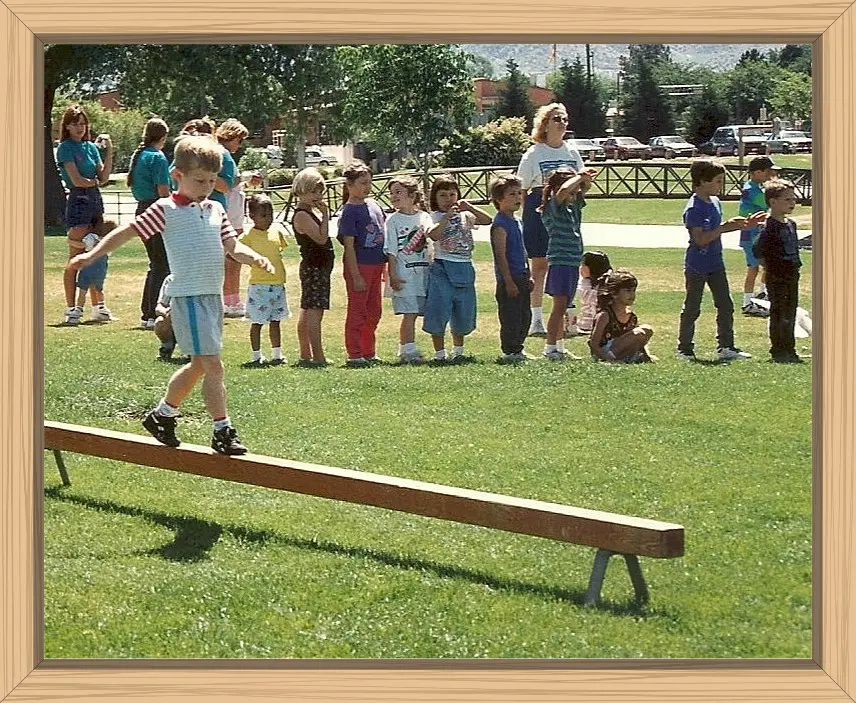 Hayes was working on his balance, walking on a low-to-ground wooden balance beam. His teacher and classmates are in the background.