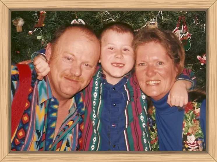 Pete, Hayes, and me in front of our Christmas giving a three way hug. Hayes is missing his two front teeth because he was about eight years old in this photo.