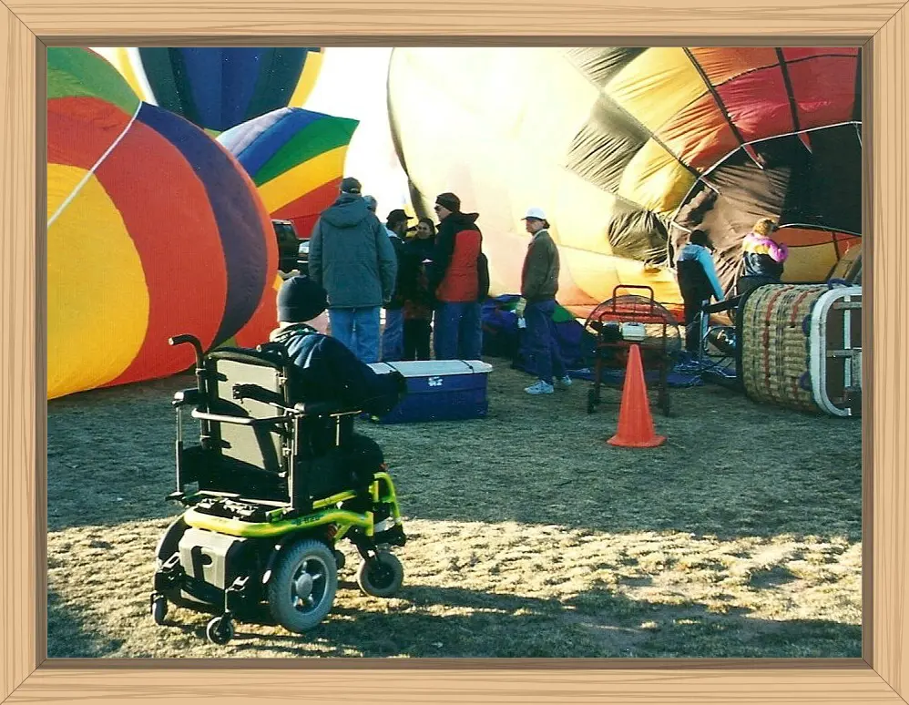 Hayes in his power wheelchair between two hot air balloons that are inflating.